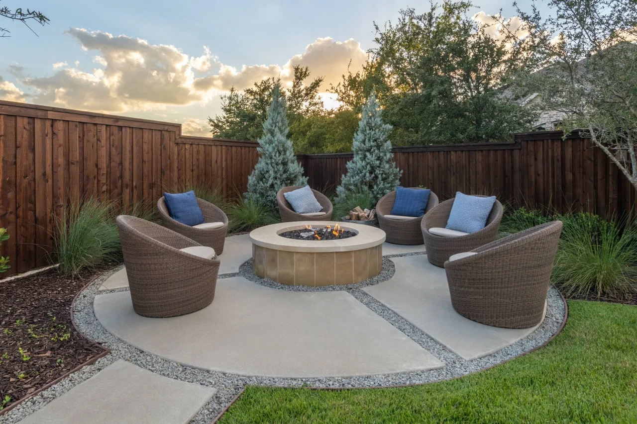 Concrete patio with a fire pit and seating behind a home with a wood privacy fence