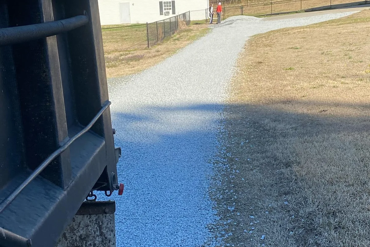 Dump truck tailgate spreading crushed limestone down a residential driveway