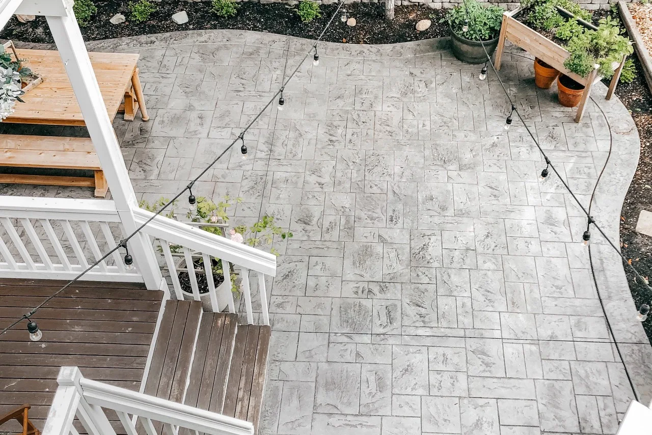 Gray ashlar slate stamped concrete patio behind a home with a deck and string lights